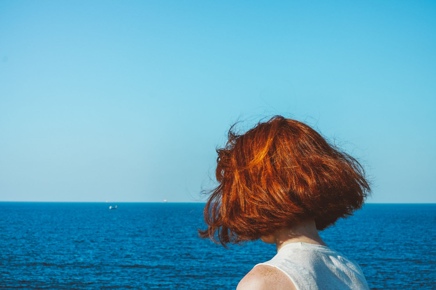 Mulher de frente para o mar com cabelo sob o sol