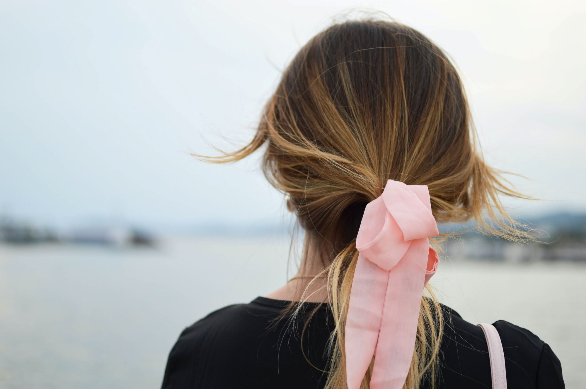mulher de costas, com cabelo fino e arramado em uma fita rosa